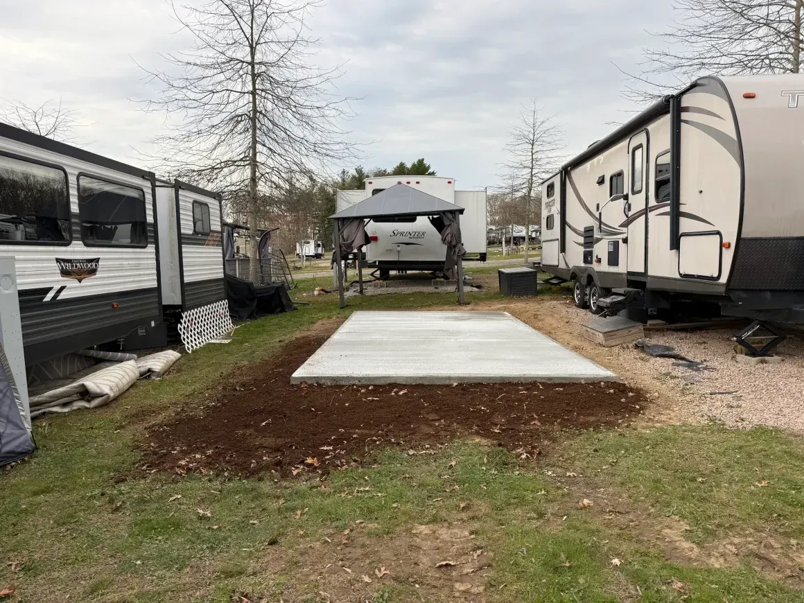 RV campsite with two trailers, a concrete pad, and a picnic shelter in the background