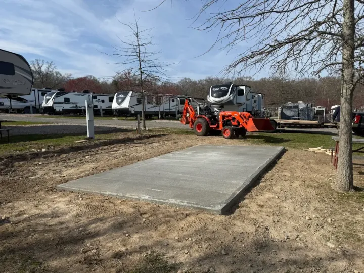 Orange tractor working near a concrete pad at a park or worksite, with parked vehicles in the background