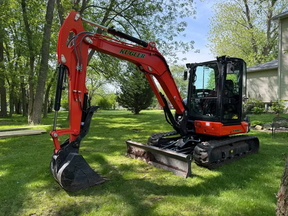 Red excavator parked on a grassy lawn beside trees and a house