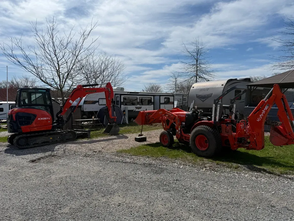 Two red tractors and an excavator parked on gravel under a cloudy sky