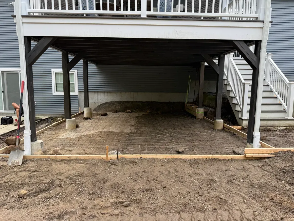 Raised deck under construction with gravel base, black support posts, and staircase on the right