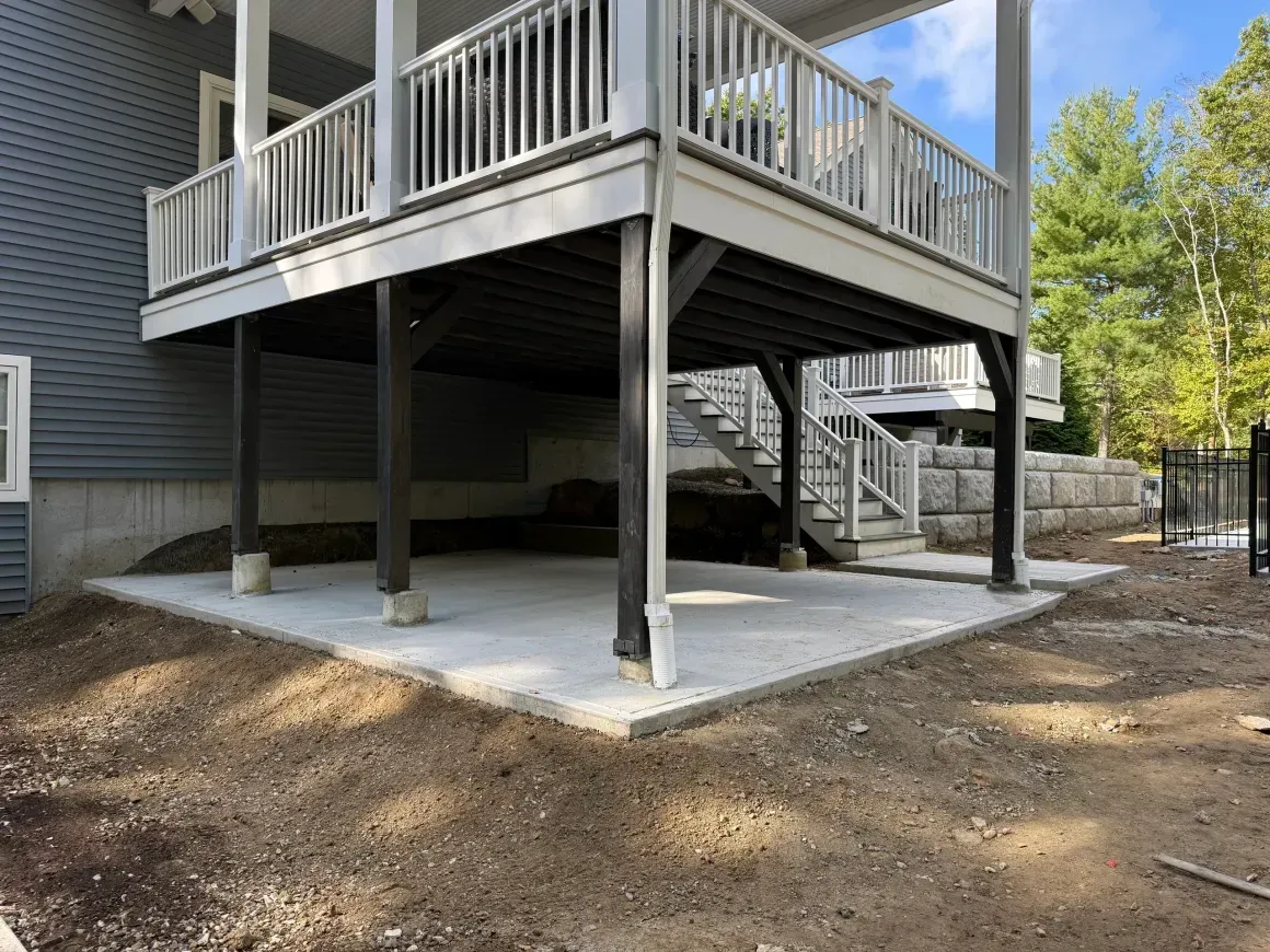 Raised wooden deck with stairs and railing over a concrete patio in a yard