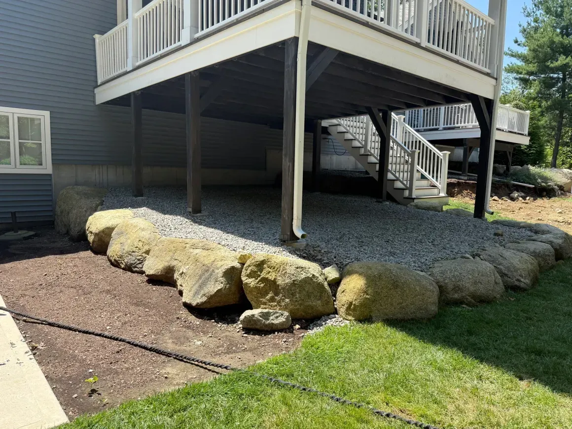 Raised wooden deck with stairs over landscaping stones and a grassy yard