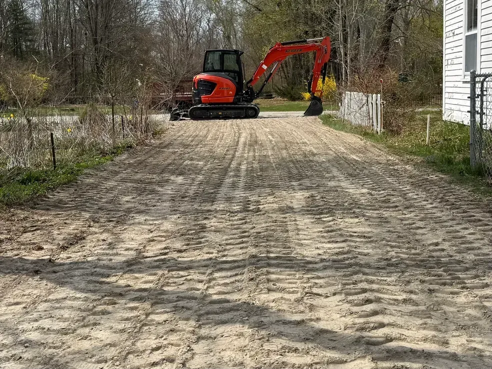 Orange excavator parked on a gravel driveway beside a house and trees
