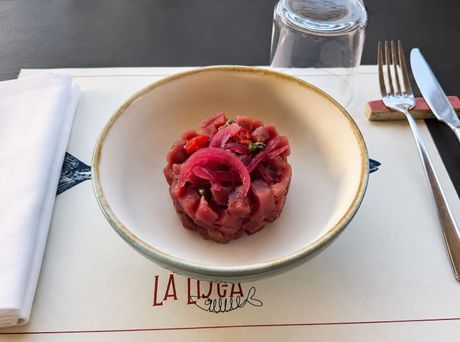 Piatto di frutti di mare: gamberi, carpaccio di pesce e tartare di tonno su un piatto blu.