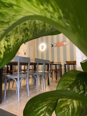 Interno di un ristorante con tavoli apparecchiati, decorazioni a forma di pesce sulle pareti e fiori.