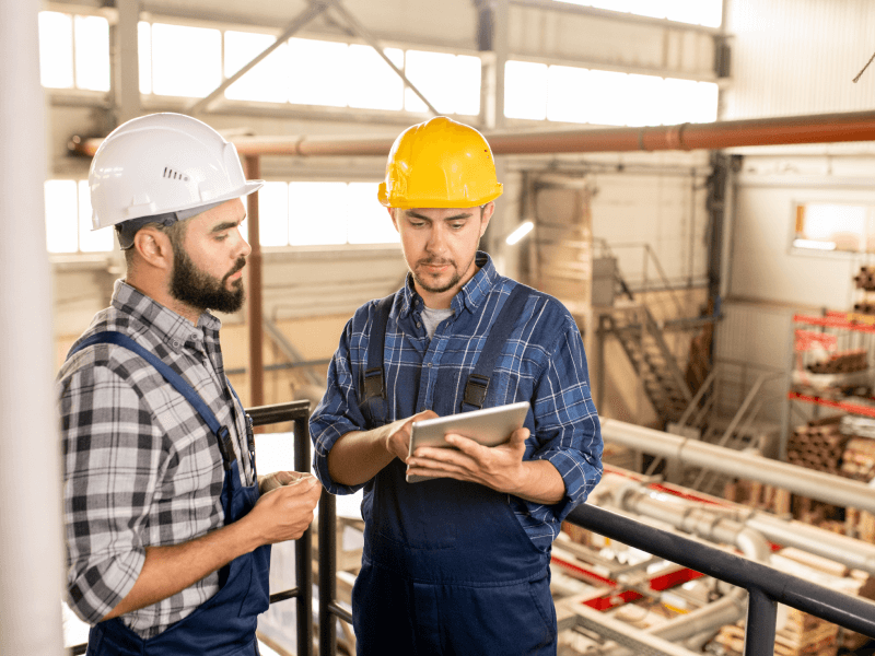 Two workers in hard hats reviewing a tablet at an industrial site