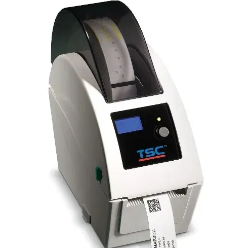 Compact desktop label printer with a roll of labels and a small display, printing a barcode tag.