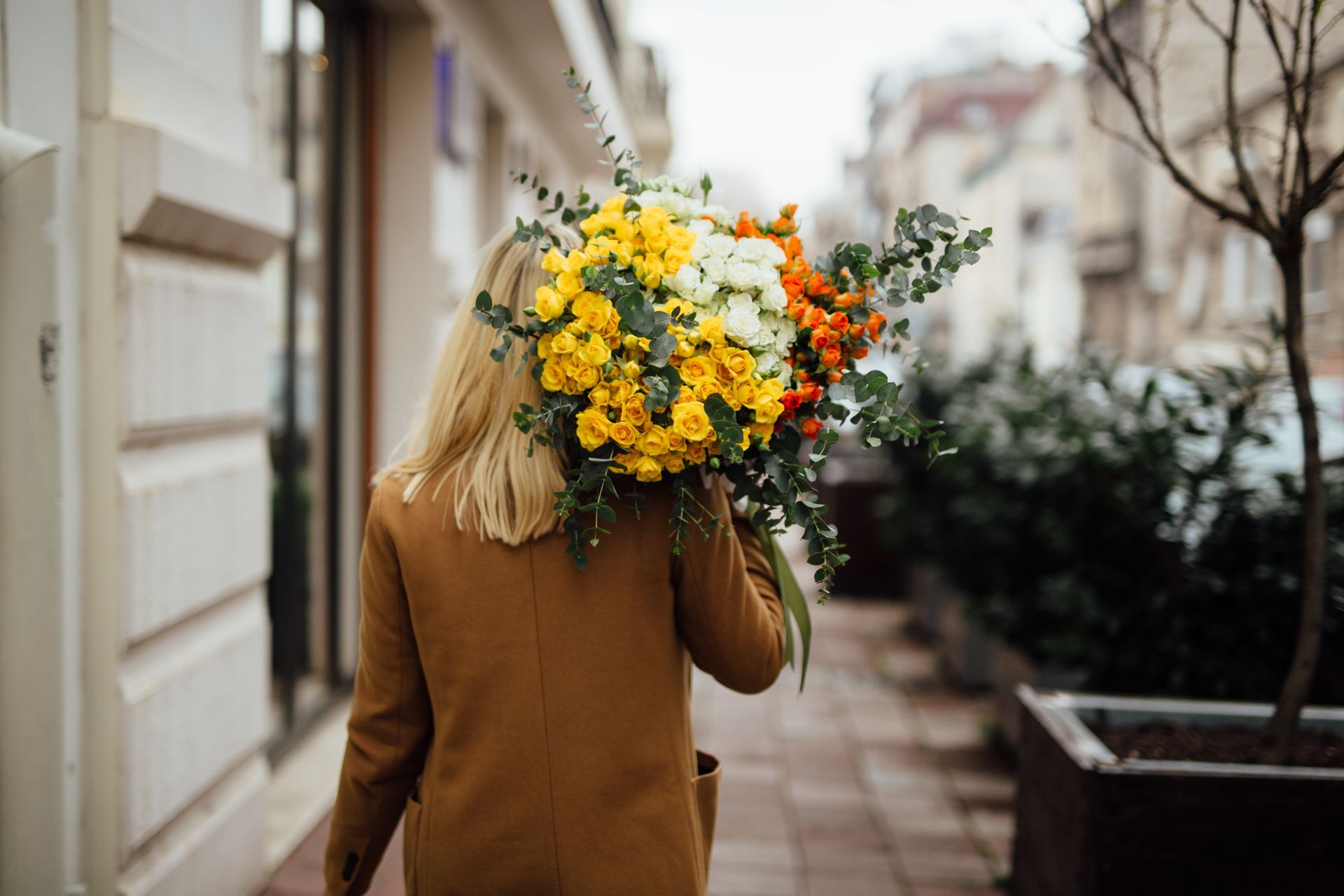 Person walking down a street carrying a large bouquet of yellow and orange flowers near Prelude at Medley.