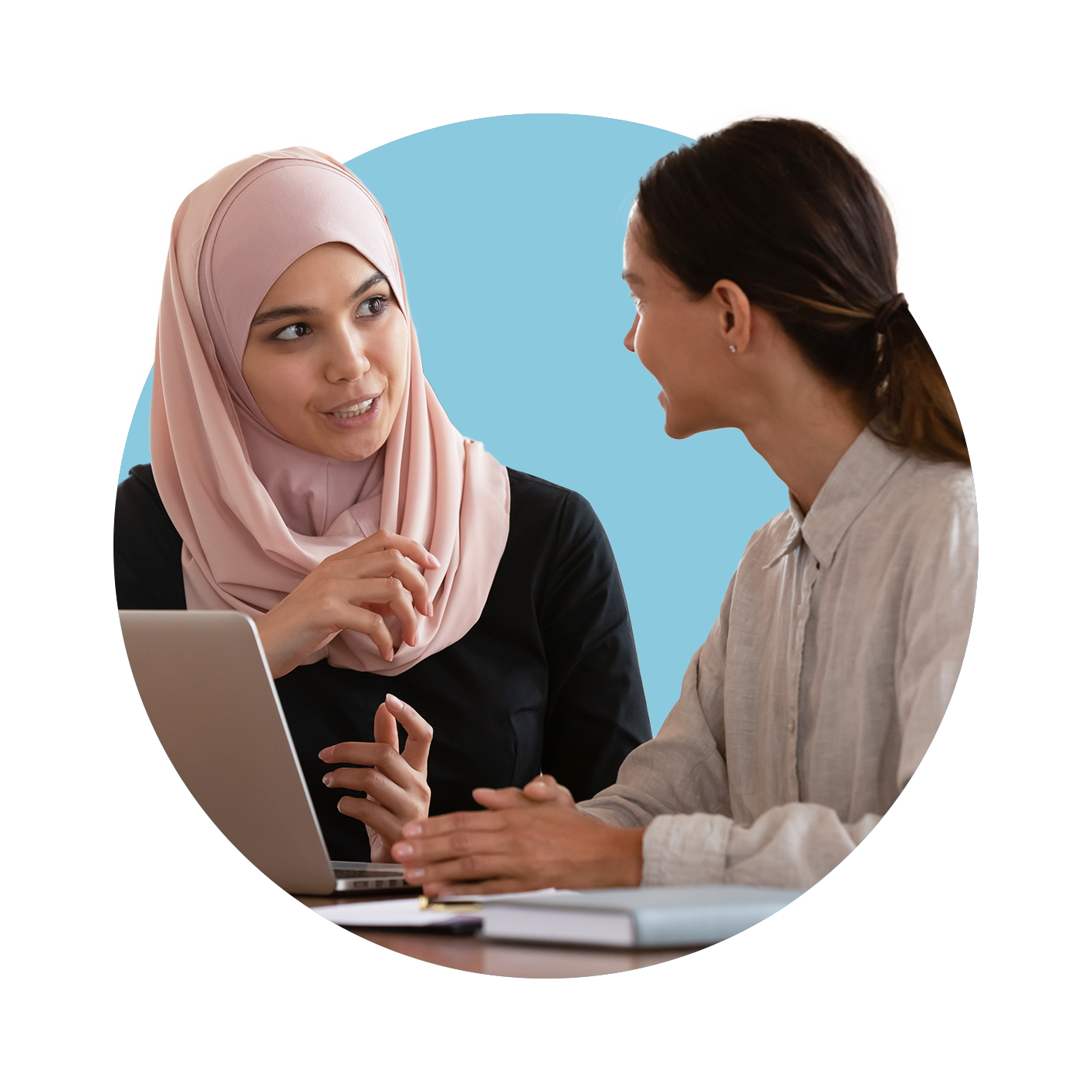 Two young woman talking to each other whilst at a laptop