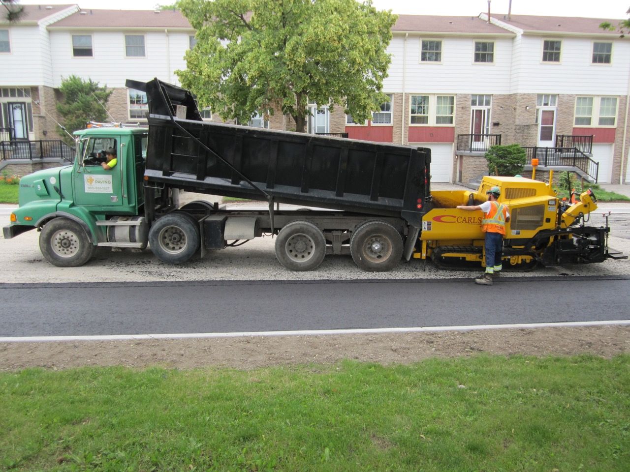 A green dump truck is parked next to a yellow truck
