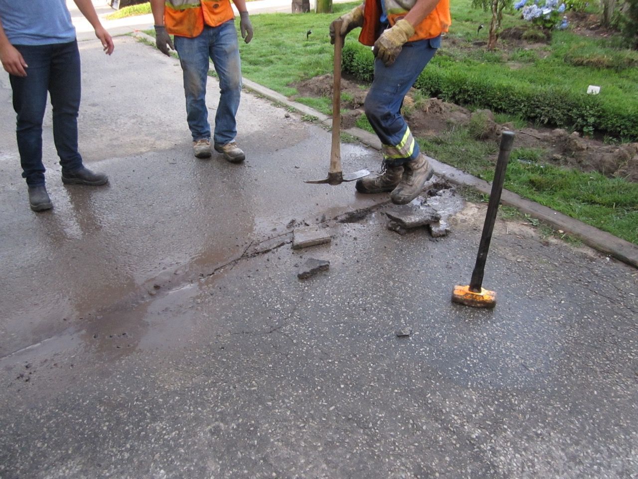 Two men are working on a sidewalk with a hammer and a broom.