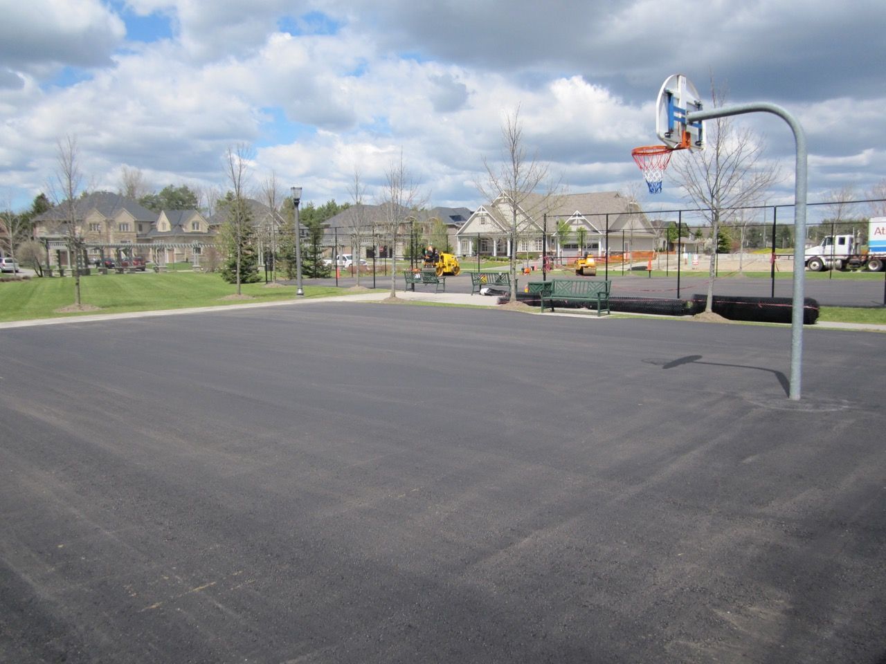 A basketball hoop in a parking lot with houses in the background