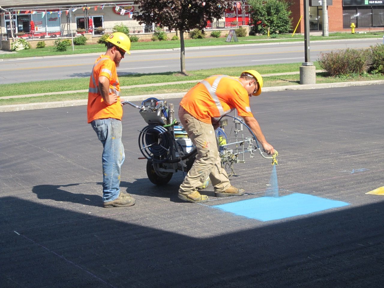 Two men are painting a blue square on the road