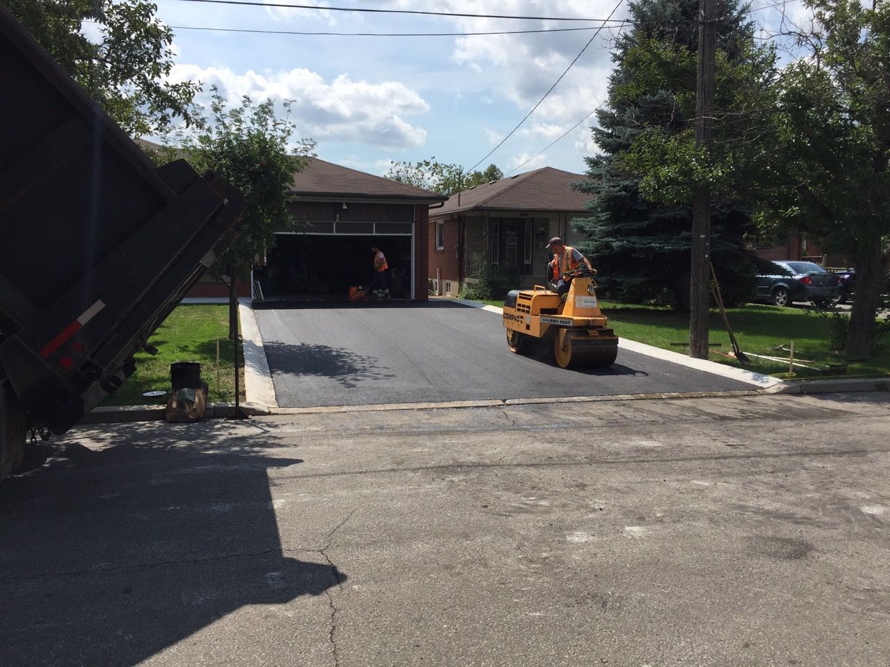 A man is driving a yellow roller down a driveway in front of a house.