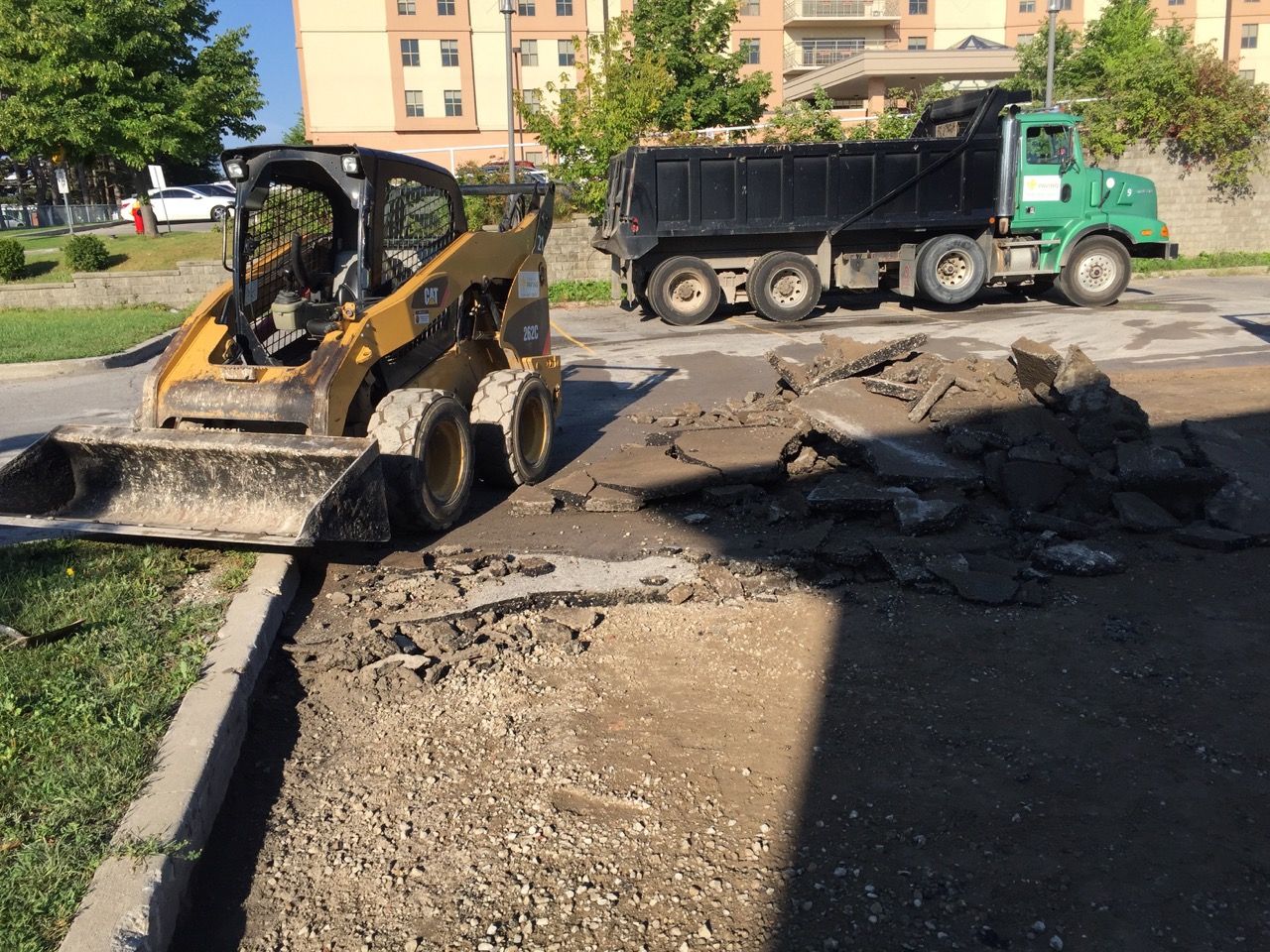 A dump truck is parked next to a bulldozer on the side of the road.