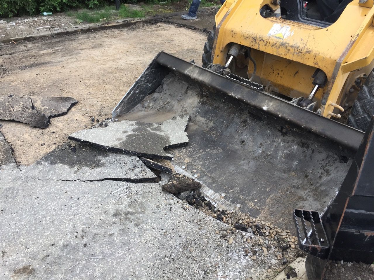 A bulldozer is breaking up a concrete driveway.