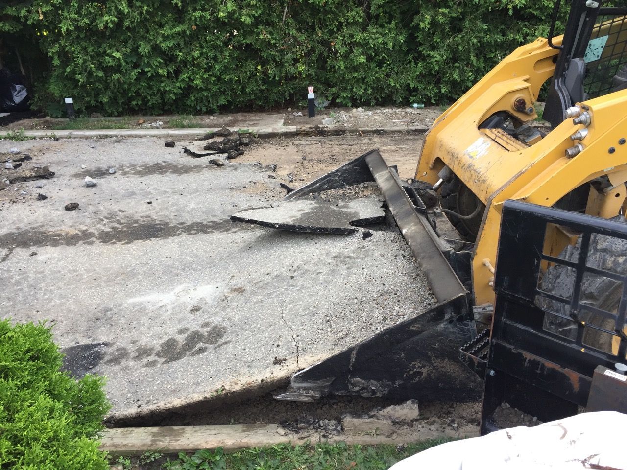 A yellow bulldozer is working on a concrete driveway.