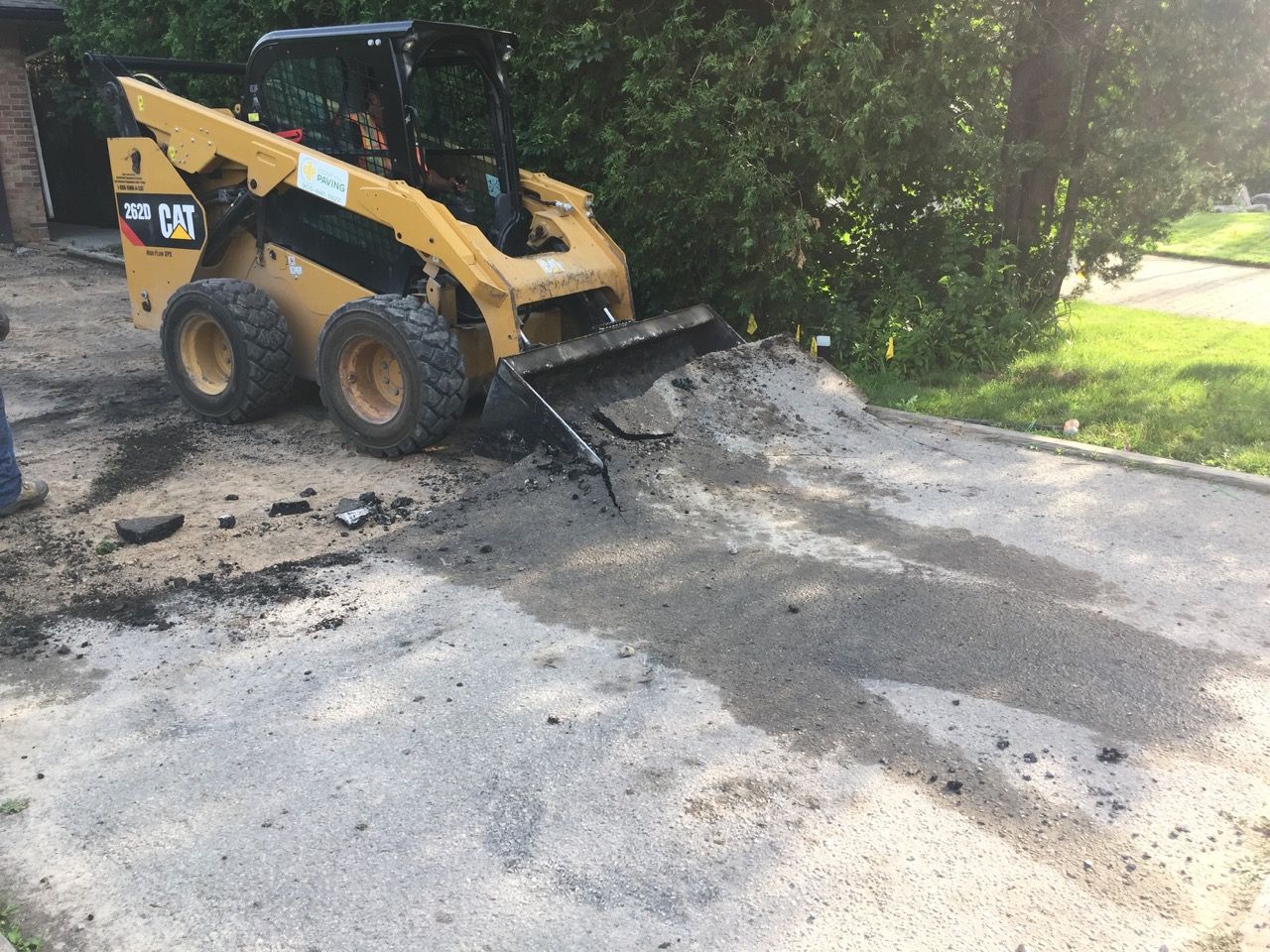 A cat skid steer is moving dirt in a driveway.