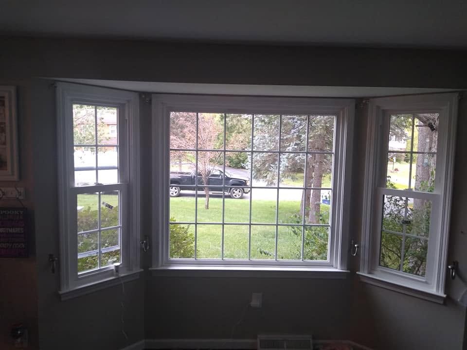 Empty living room bay window with white trim overlooking a grassy front yard and parked car