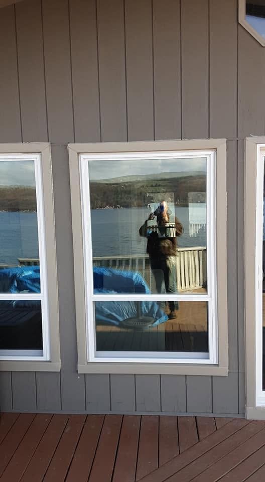 Person reflected in a window of a gray-sided building with white trim and a wood deck.
