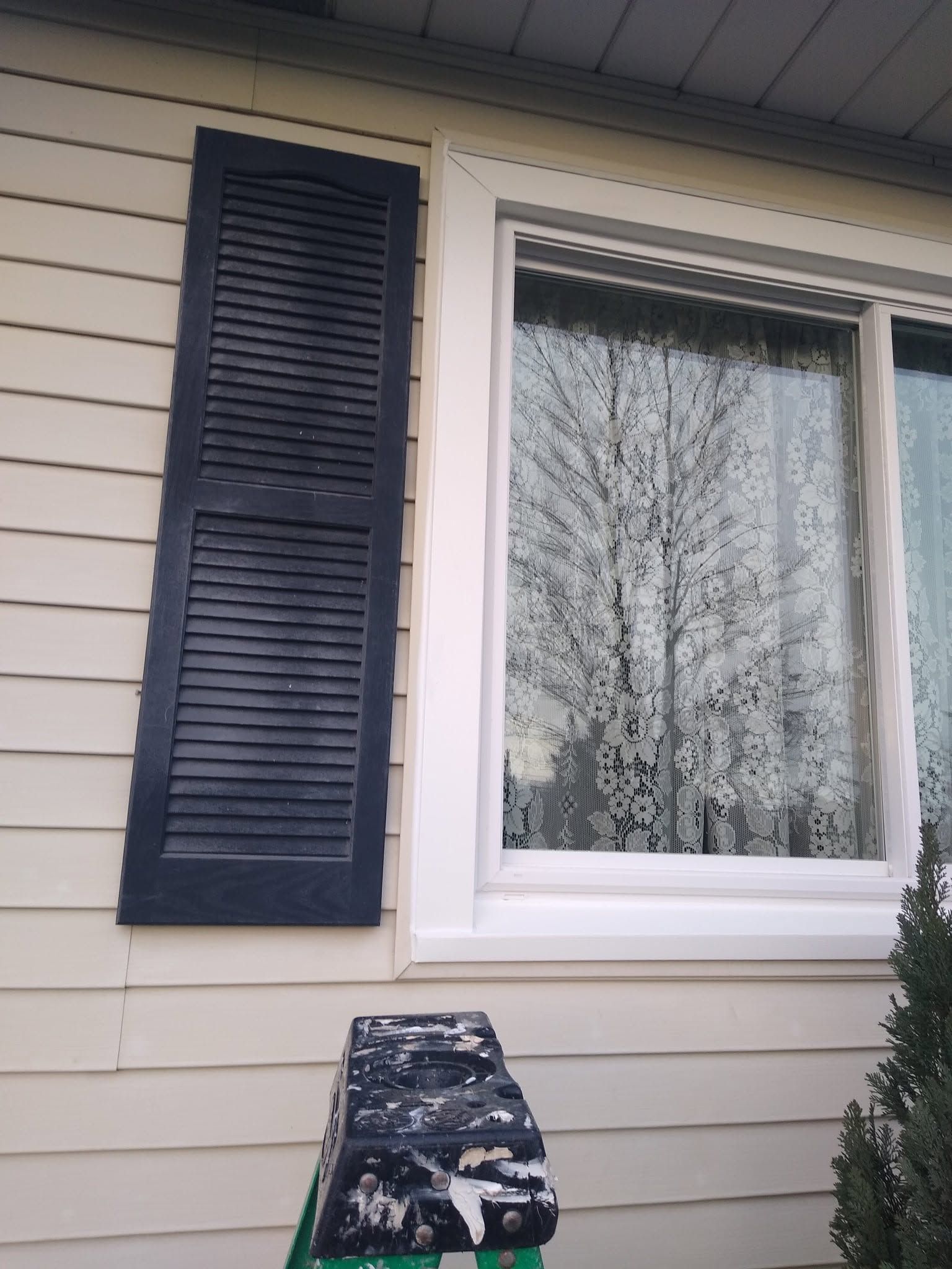 House exterior with a white-framed window and a dark blue shutter beside beige siding.