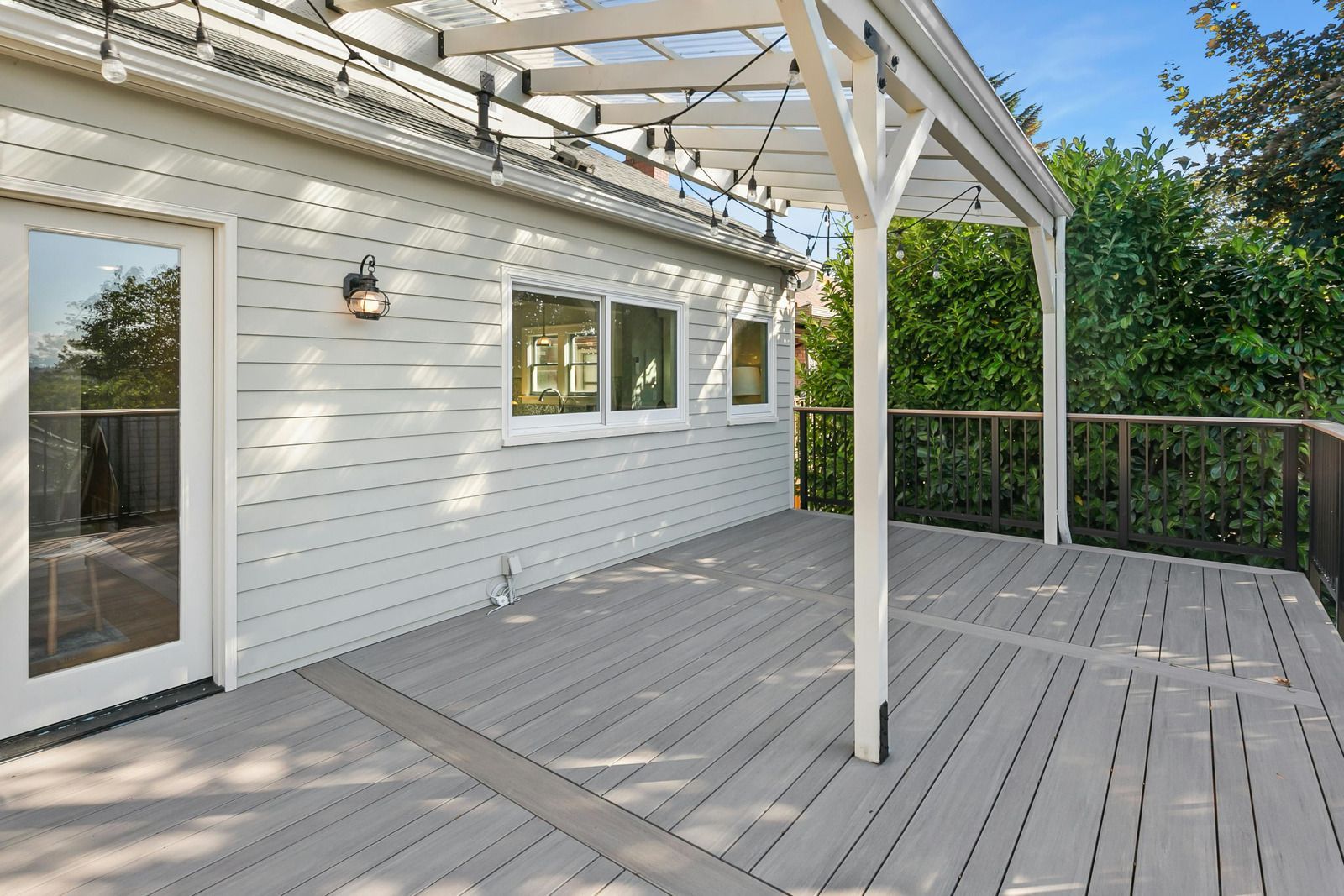 White house deck with sliding glass door, windows, and pergola over weathered gray boards