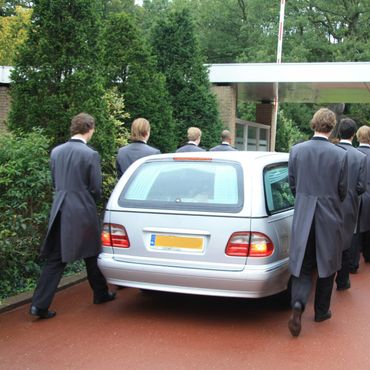 Un grupo de hombres de traje camina hacia un coche plateado.