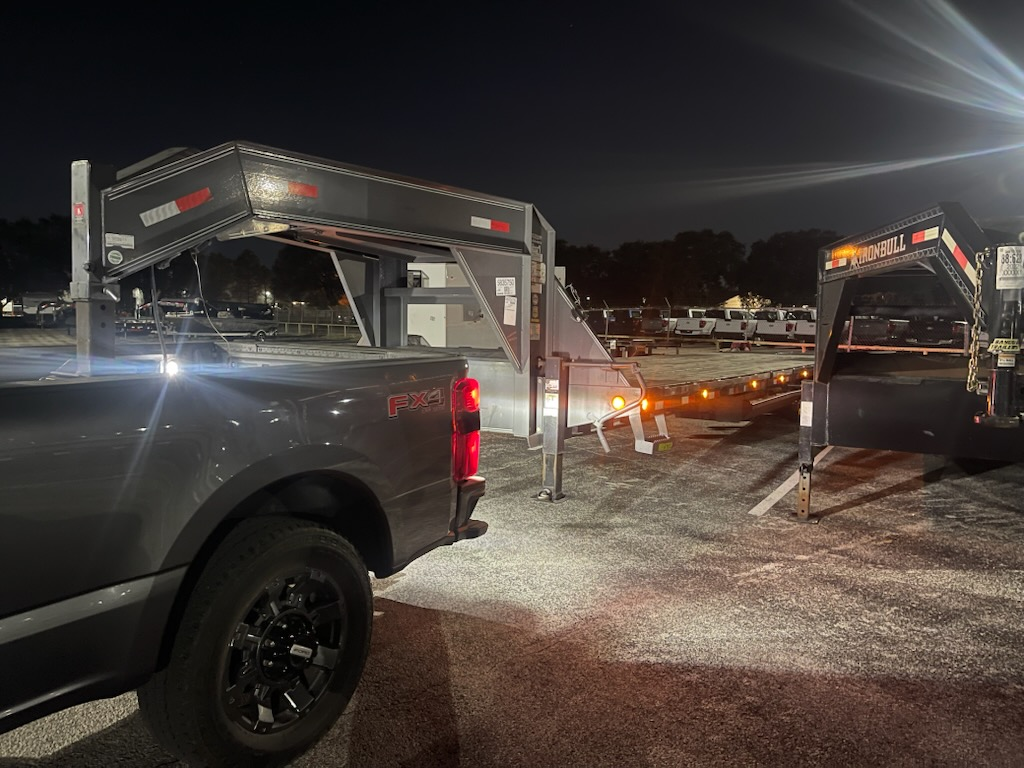 A truck with a trailer attached to it is parked in a parking lot at night.
