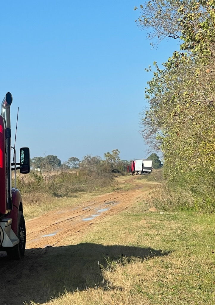A red semi truck is parked on the side of a dirt road.