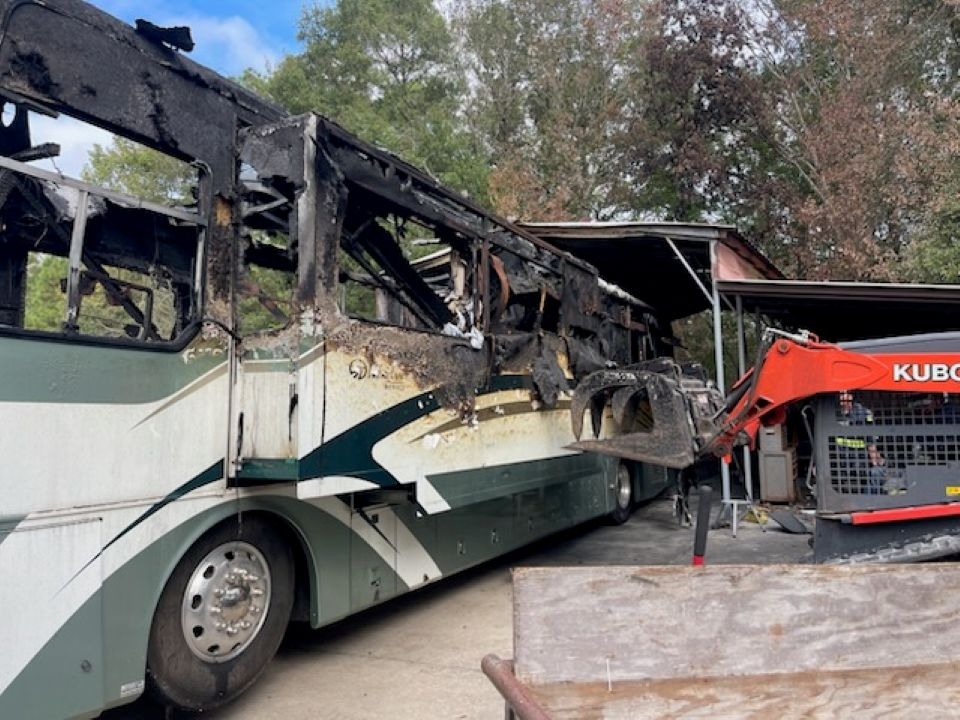 A kubota excavator is parked next to a rv that has been damaged in a fire.