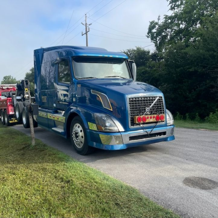 A blue volvo semi truck is towed by a red tow truck