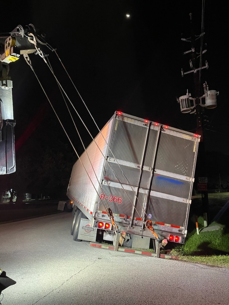 A semi truck is being towed by a crane at night.