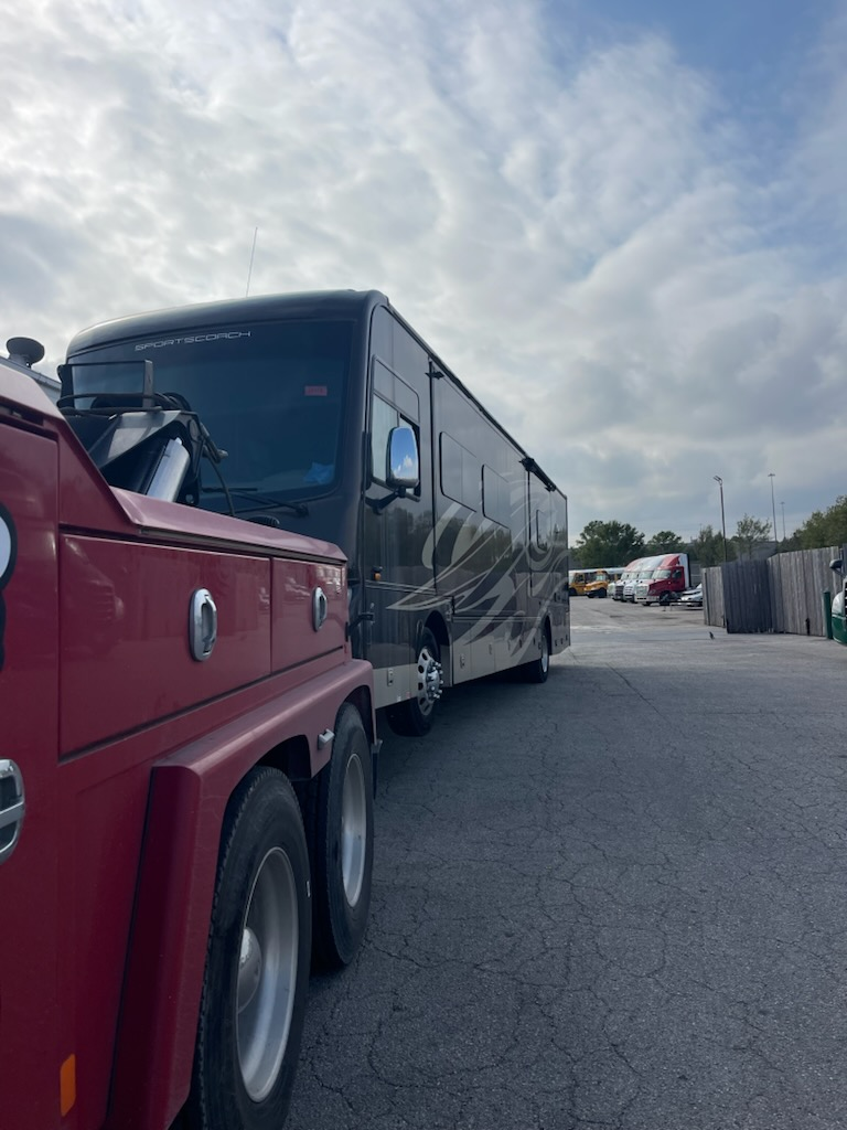 A red tow truck is towing a large rv in a parking lot.