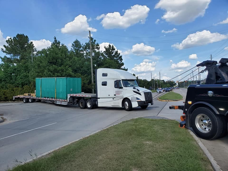 A red shipping container is being lifted by a crane on top of a semi truck.