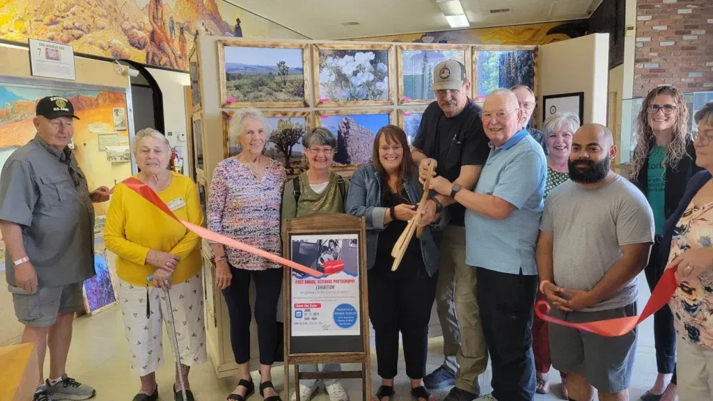 Group of people cutting a ribbon at an art gallery opening. Artwork hangs on the wall behind them.