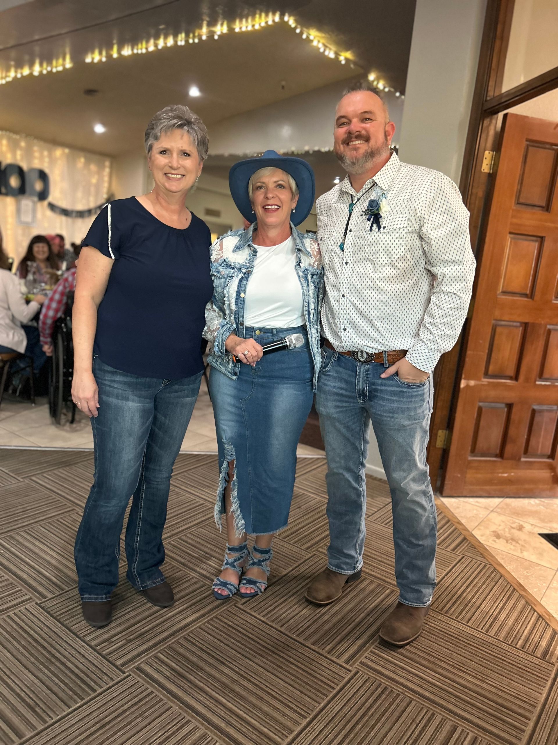 Three people in denim clothing smile inside a building.