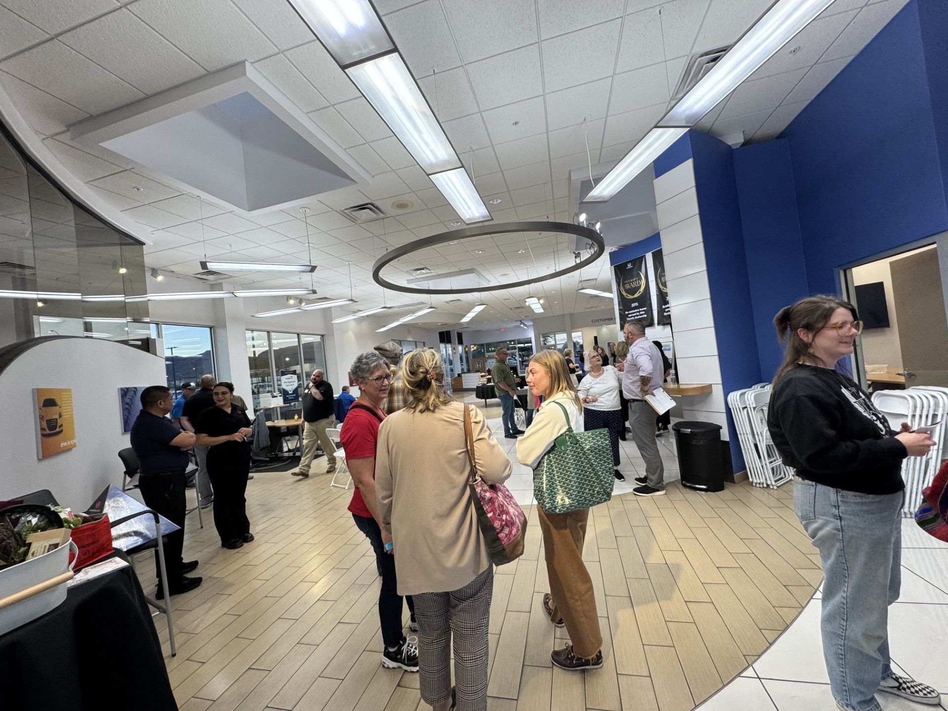 People gather inside a bright, modern space. Wooden floors, blue walls, overhead lights, and a large circular fixture.