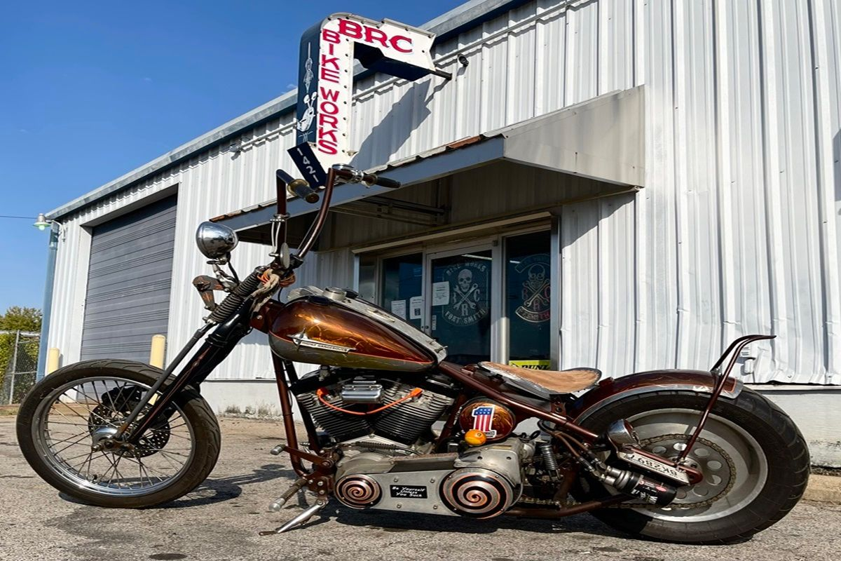Black Harley-Davidson motorcycle parked in a showroom, chrome exhaust pipes, and black wheels.