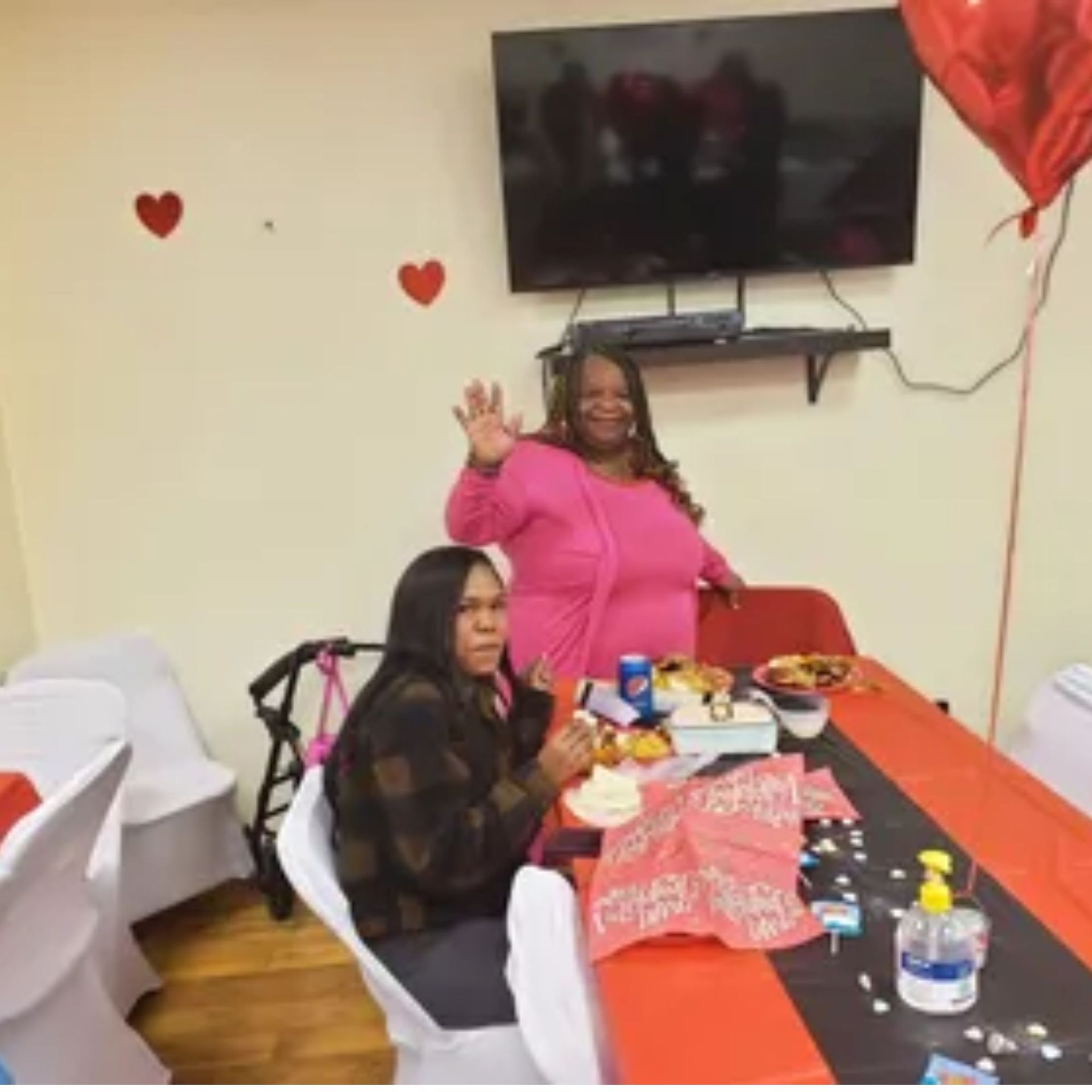 Two women sitting at a table in front of a flat screen tv