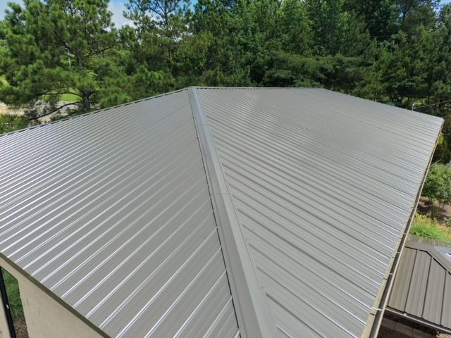 Gray metal roof with standing seams, viewed from above, surrounded by trees and greenery