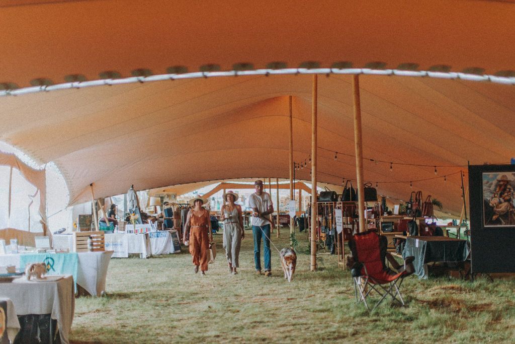 Large tent event with people standing and seated on grass under a white canopy