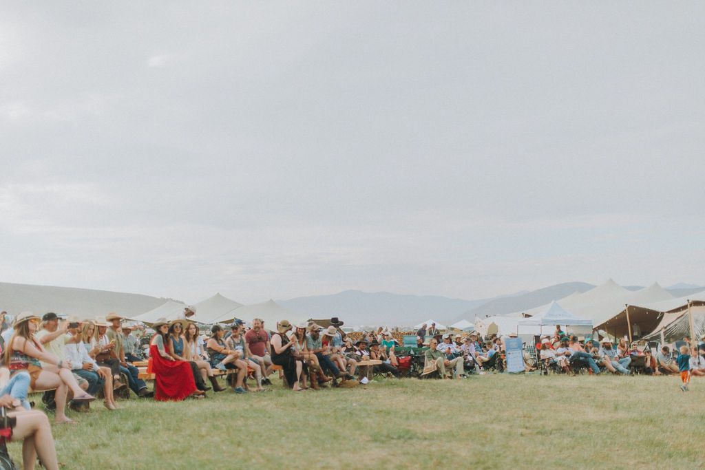 Outdoor wedding ceremony on a grassy field, with seated guests and mountains in the distance.