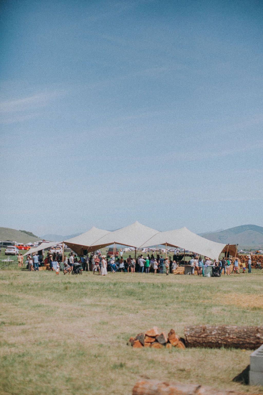 People gathered under white tents in a grassy field under a clear blue sky.