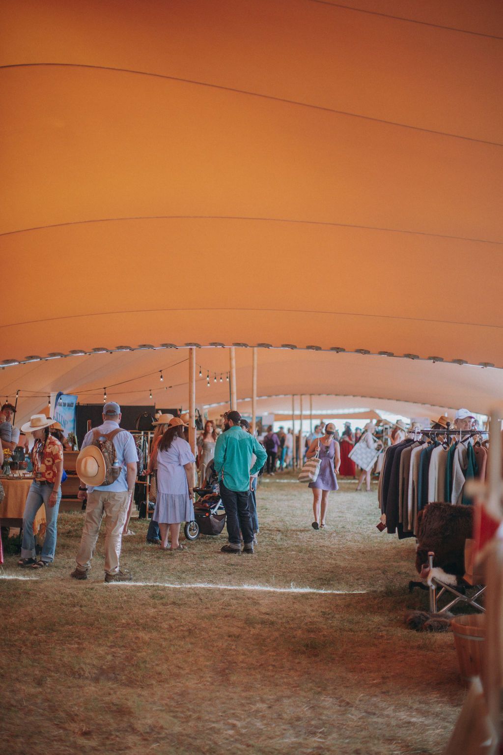 People browsing clothing racks under a large orange tent at an outdoor market.