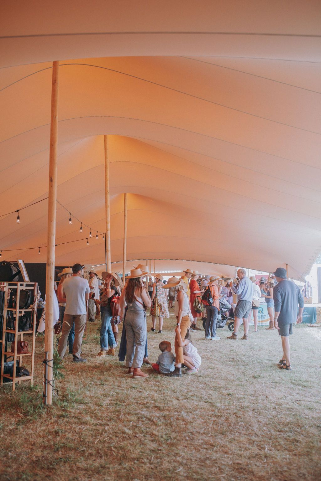 People gathered under a large white tent at an outdoor event, with warm orange lighting.