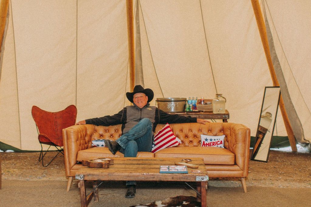 Man sitting on a tan couch inside a beige tent, surrounded by pillows and decor.