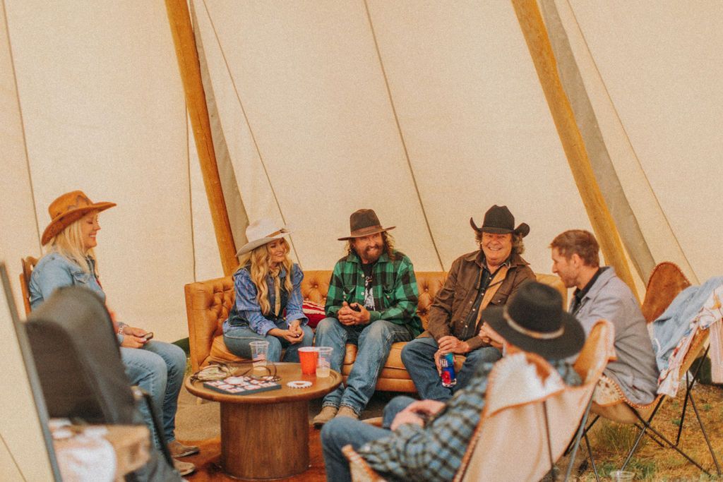 People seated around a table inside a canvas tent, chatting and drinking