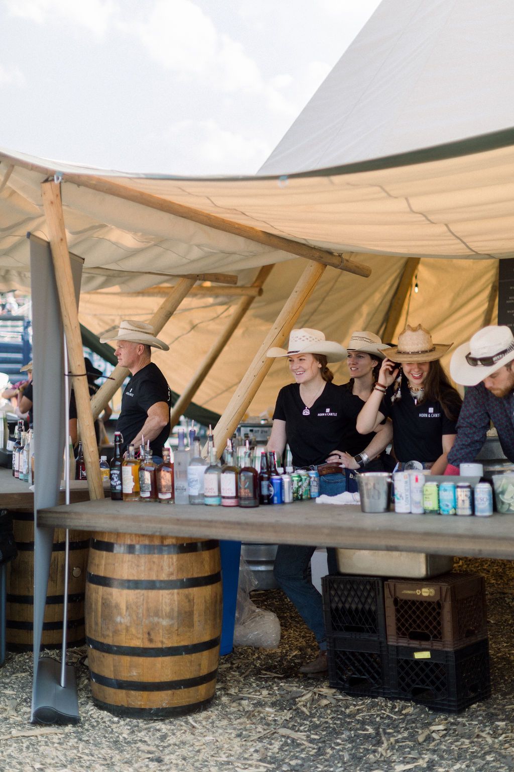 People serving drinks from a rustic outdoor bar under a canopy at a fairground