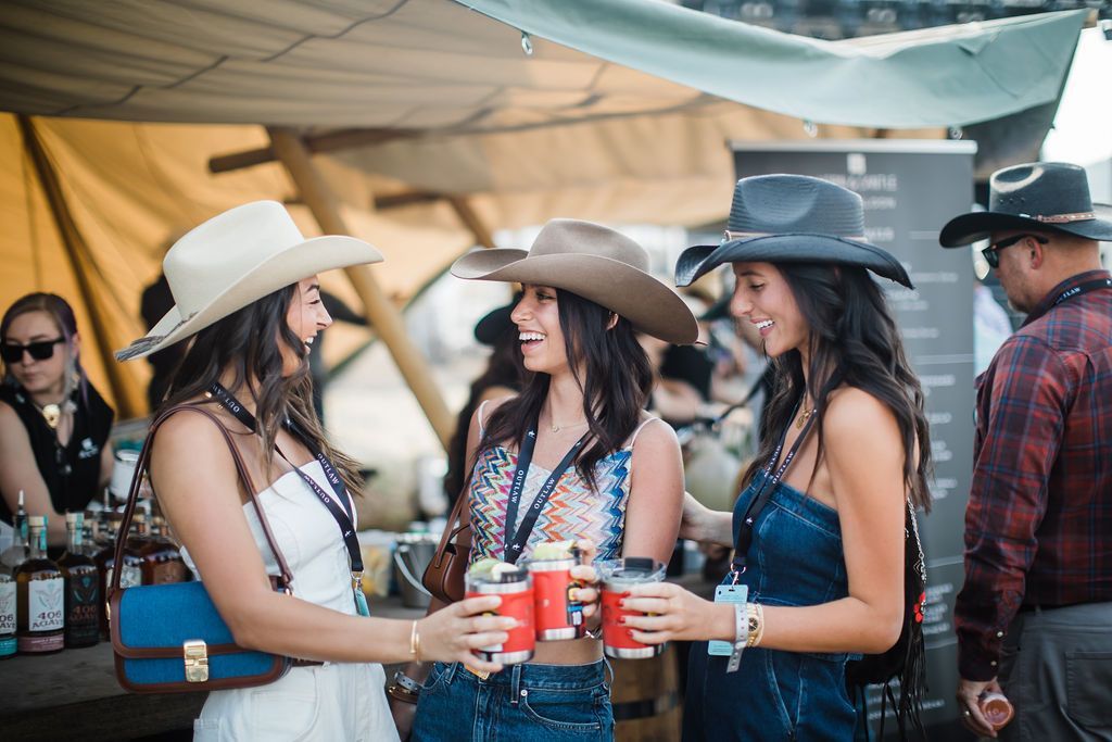 Friends in cowboy hats holding red cups at an outdoor party under a canopy